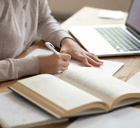 Graduate holding books and a laptop, immersed in writing a dissertation. Seeking Dissertation Introduction Writing Help for a comprehensive and effective academic start.