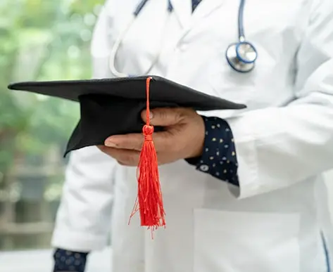 Doctor studying and learning in a hospital ward, wearing a graduation cap, symbolizing achievement in the field of medicine. Illustrates a clever and bright genius in medical education. Relevant for those seeking nursing dissertation help and exploring concepts in healthcare and education.